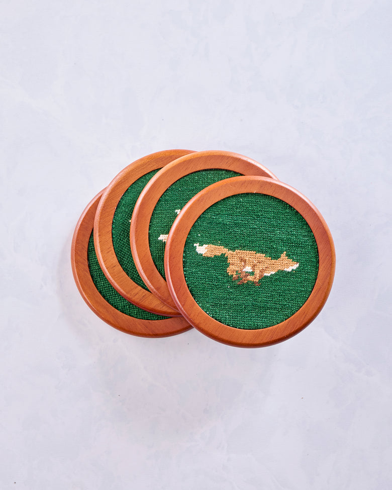 Four wooden Fox Chase coasters overlapping in a stack, with green needlepoint surfaces and a fox design on the top coaster.