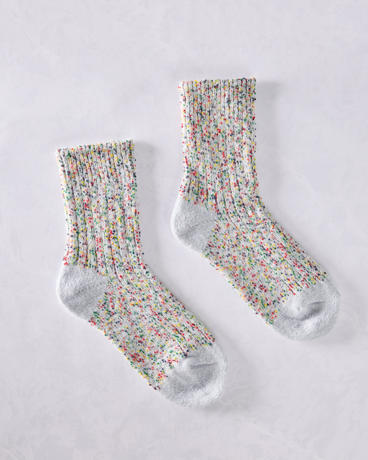 Pair of light gray short crew socks with a multicolored speckled pattern, displayed separately.