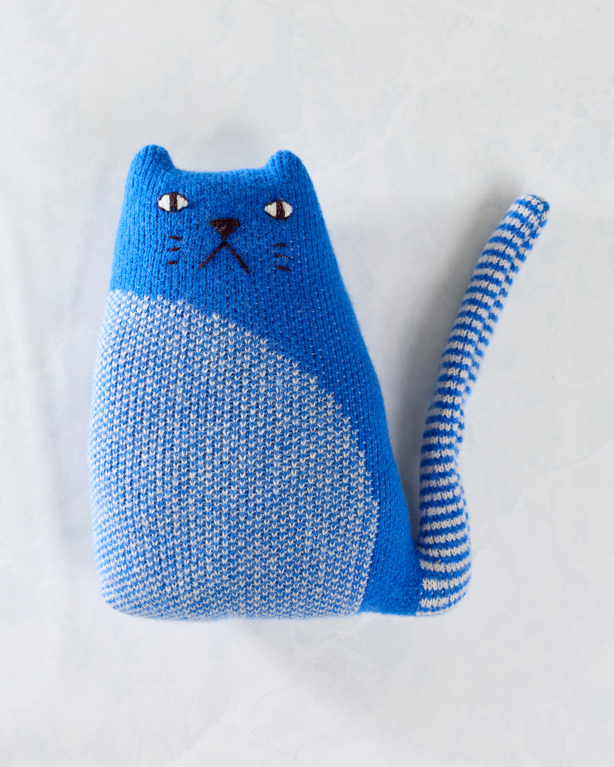 Blue knitted cat toy with a white-and-blue striped belly and tail, embroidered face, and upright ears.