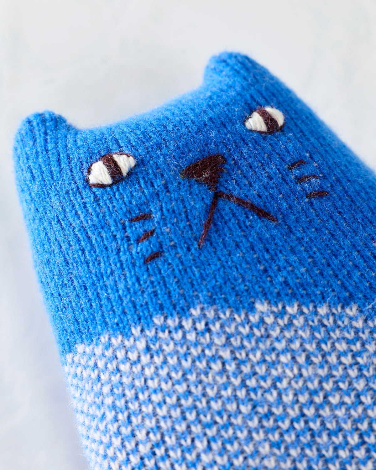 Close-up of the knitted cat toy's embroidered face and blue-and-white striped body.