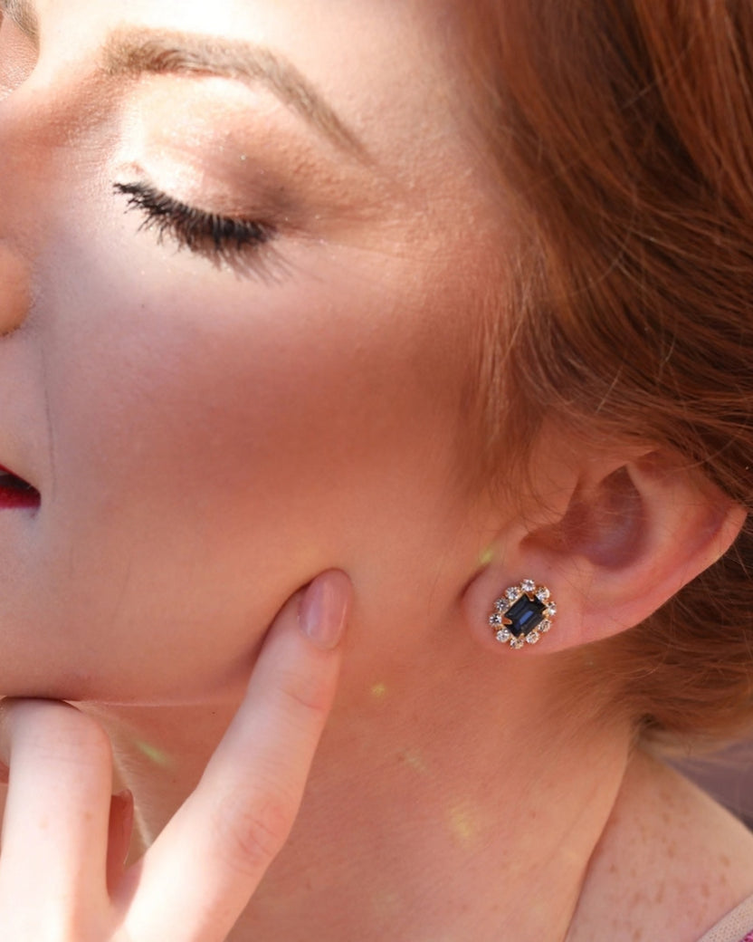 Close-up of an ear wearing a rectangular dark green stud earring surrounded by clear stones.