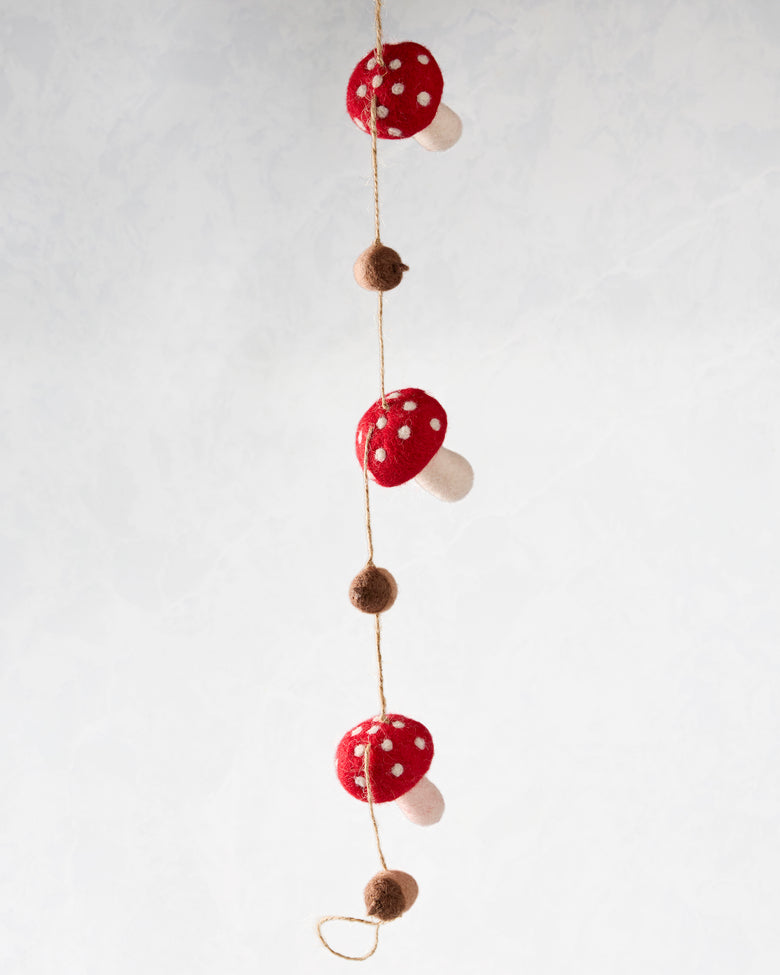 Mushroom and acorn felt garland hanging vertically, with red white-spotted mushrooms and brown acorns on a string.