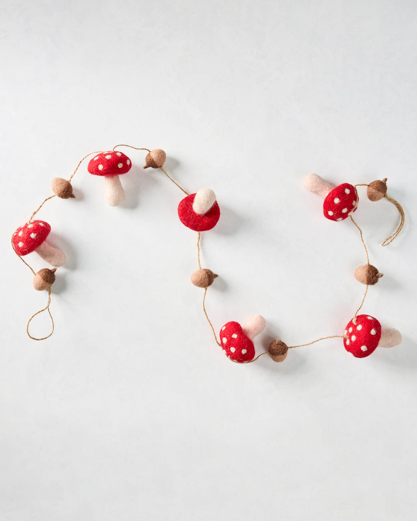 Mushroom and acorn felt garland arranged in loose curves, showing red white-spotted mushrooms and brown acorns.
