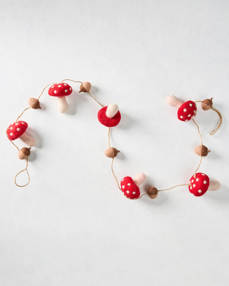 Mushroom and acorn felt garland arranged in loose curves, showing red white-spotted mushrooms and brown acorns.