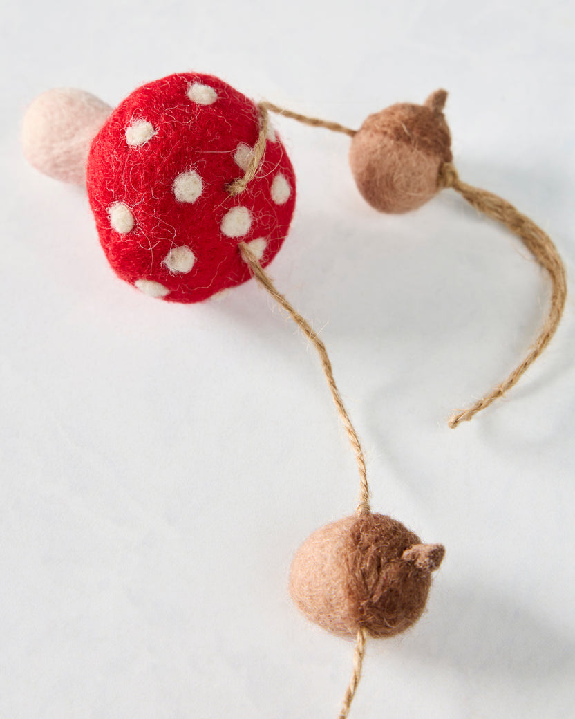 Close-up of a red white-spotted felt mushroom and two brown acorn shapes connected by string.