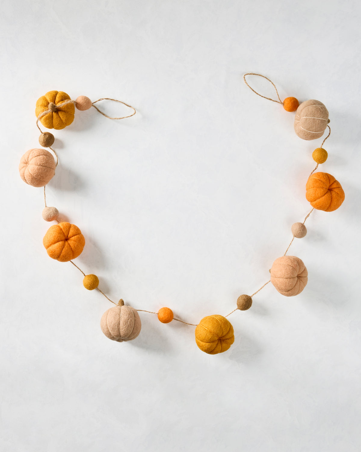 Felt pumpkin garland arranged in a loop, with orange, yellow, and neutral pumpkins and smaller felt balls on natural-colored string.