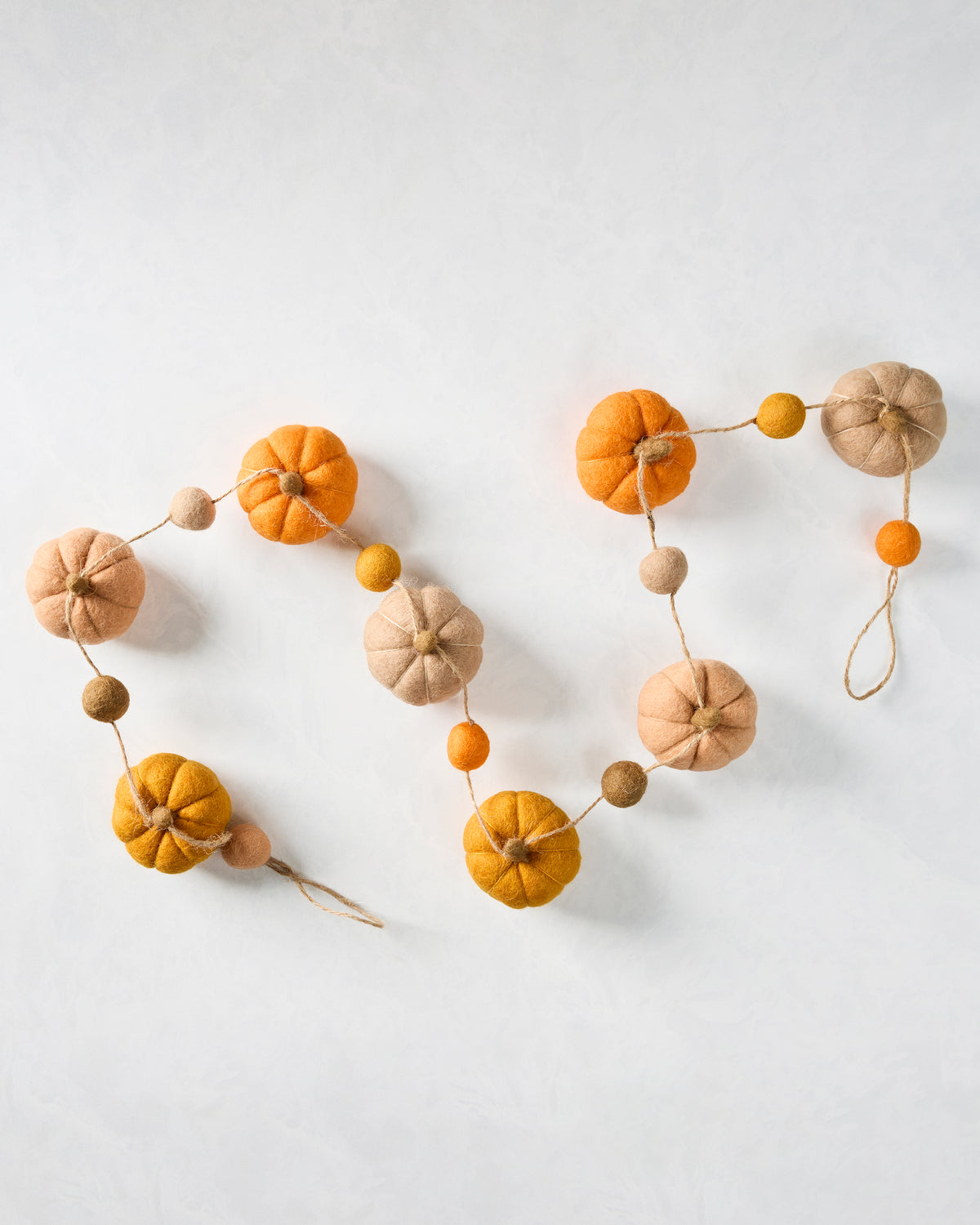 Felt pumpkin garland arranged in a loose S shape, showing orange, yellow, and neutral pumpkins with smaller felt balls on string.