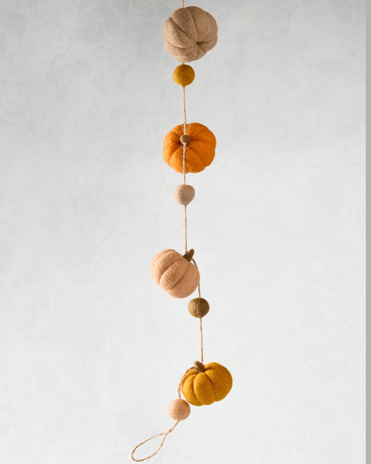 Vertical view of a felt pumpkin garland with orange, yellow, and neutral pumpkins separated by smaller felt balls on string.