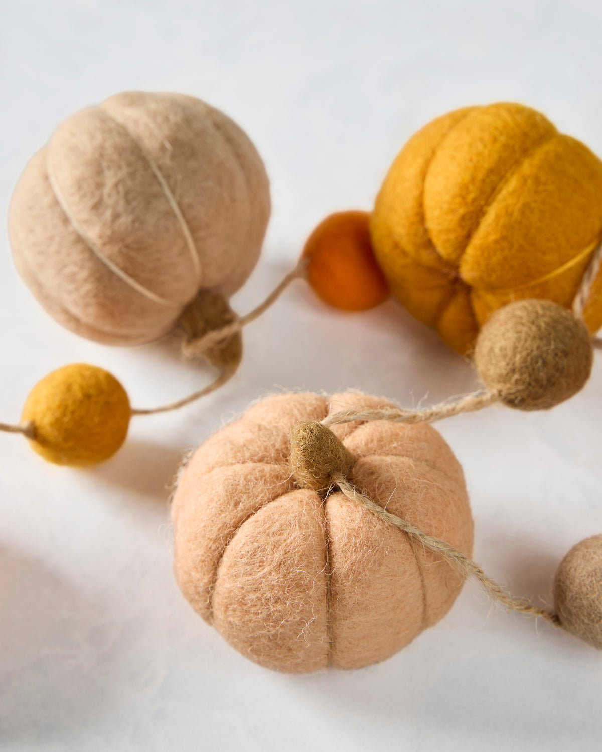 Close-up of a peach-colored felt pumpkin on the garland, with orange and neutral pumpkins and felt balls in the background.