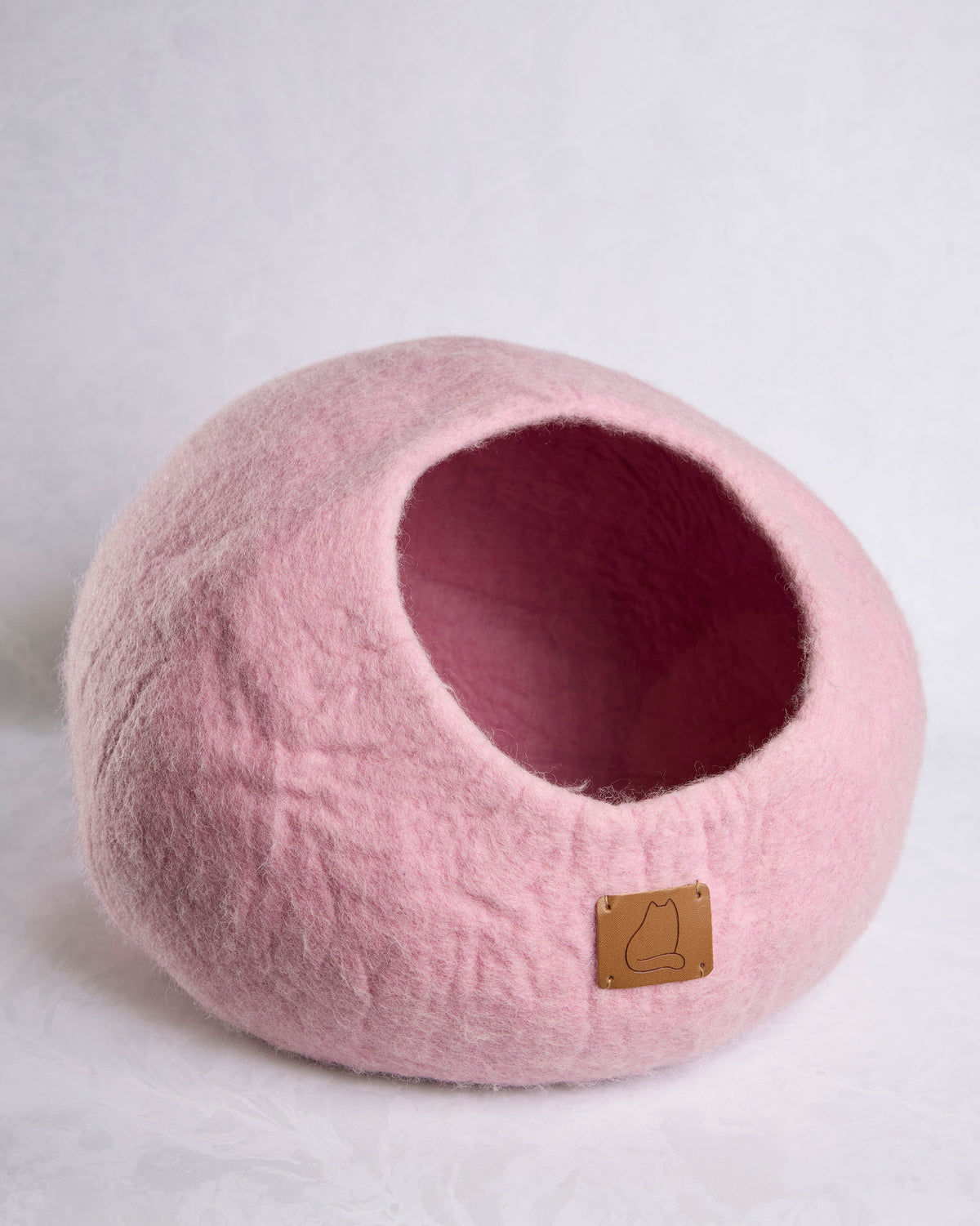 Pink felted wool cat cave bed viewed from the front, showing the round opening and leather cat-logo tag.