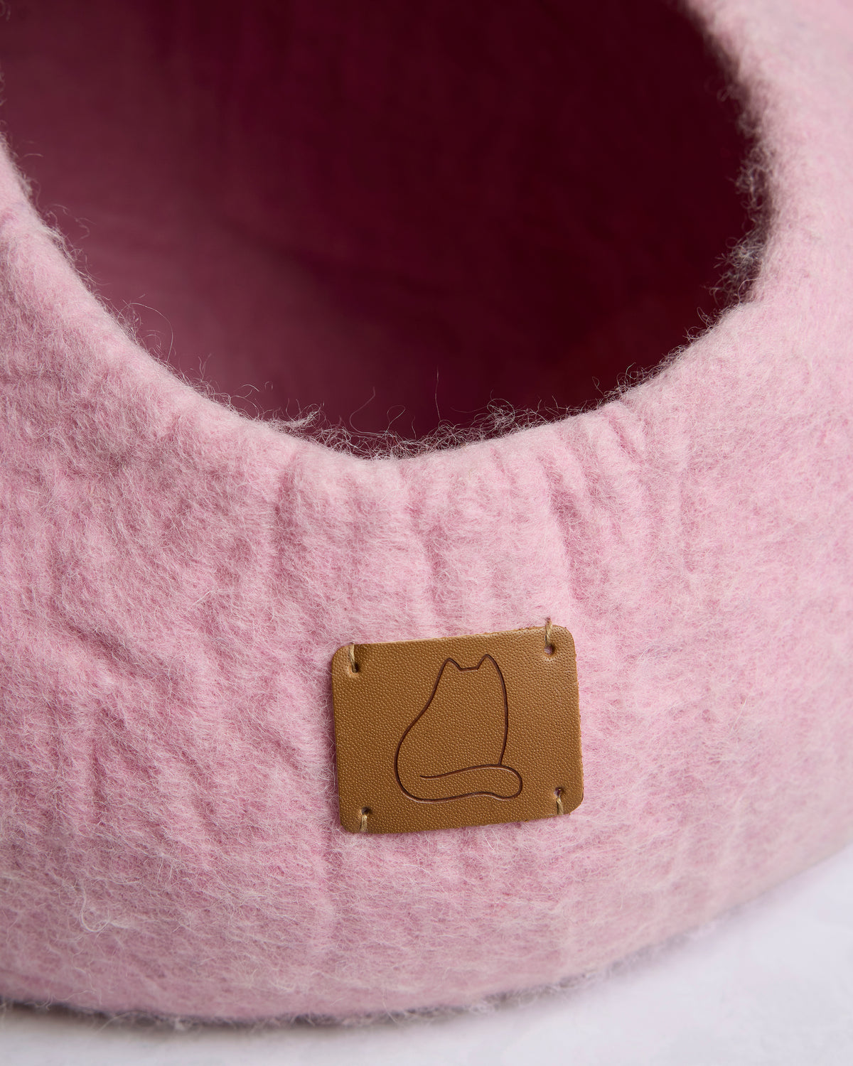 Close-up of the pink cat cave bed’s opening and brown leather tag with a cat outline.