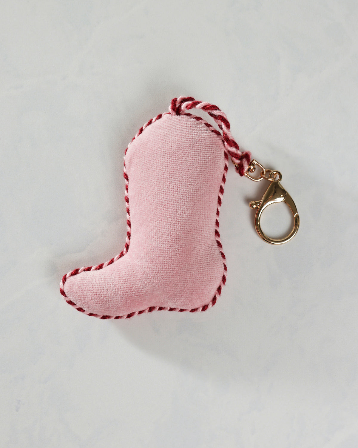 Pink cowboy boot-shaped bag charm with a red-and-white cord loop and gold clasp.