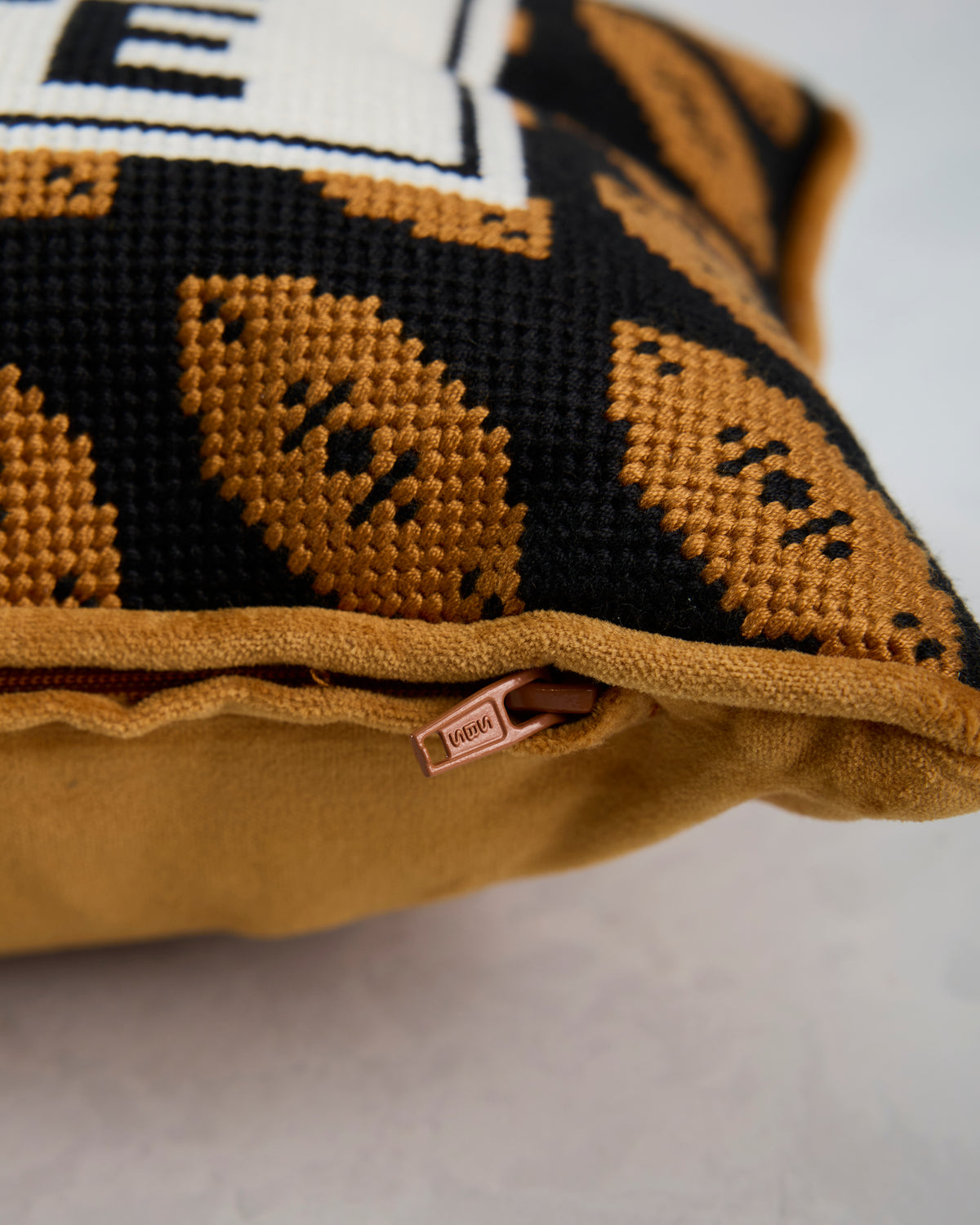 Close-up of the pillow’s patterned needlepoint edge and zipper closure.