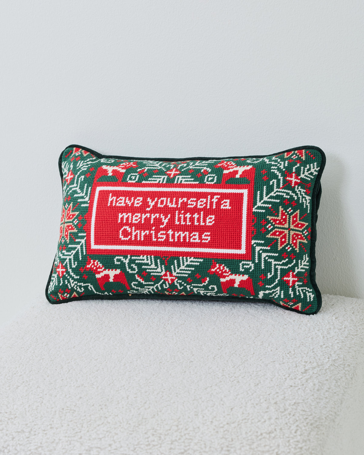 Rectangular green needlepoint pillow with red-and-white holiday motifs and the message “have yourself a merry little Christmas.”
