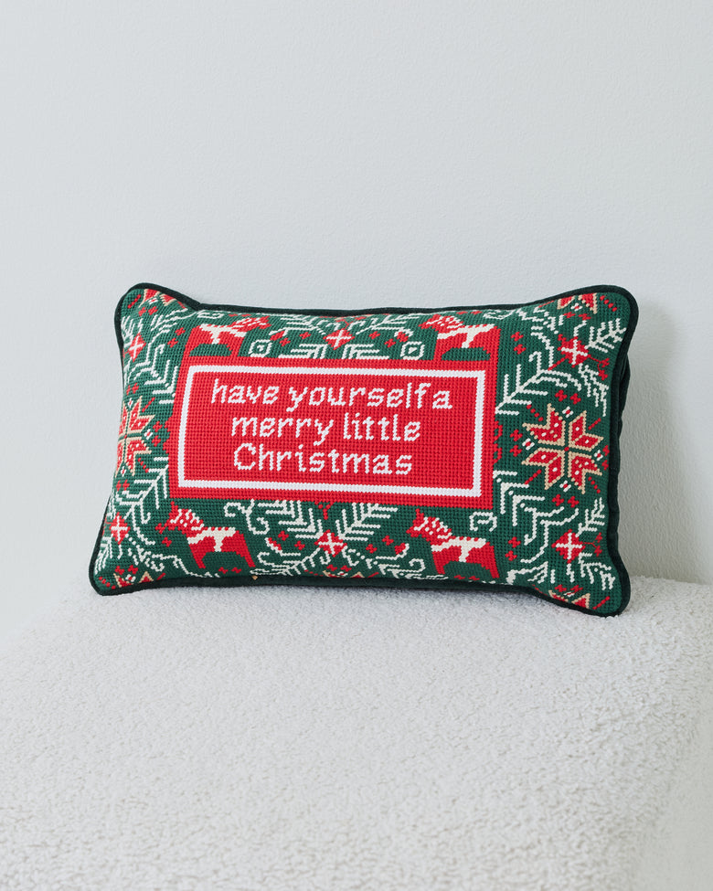 Rectangular green needlepoint pillow with red-and-white holiday motifs and the message “have yourself a merry little Christmas.”