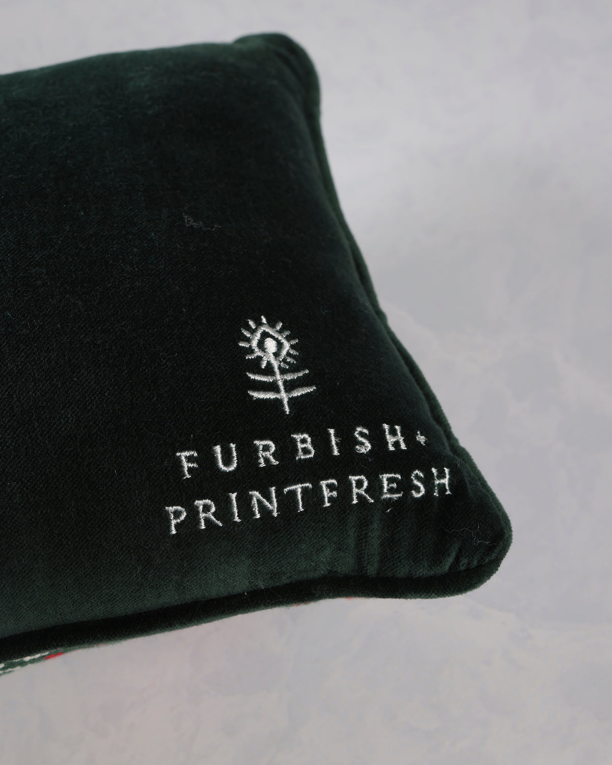 Close-up of the corner of a dark green throw pillow embroidered with the Furbish Printfresh logo.