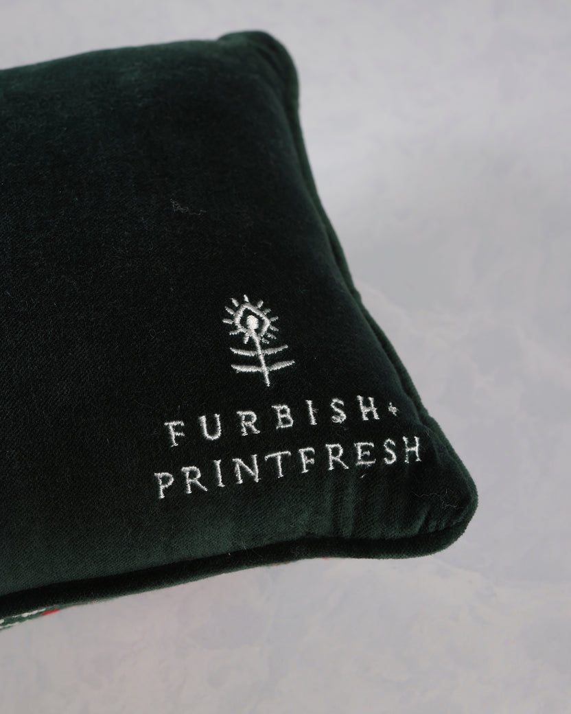 Close-up of the corner of a dark green throw pillow embroidered with the Furbish Printfresh logo.