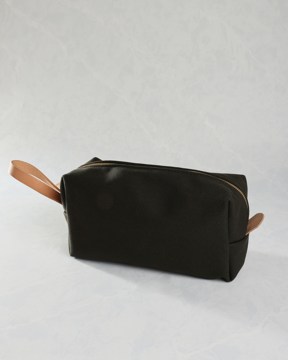 Closed black canvas travel kit with tan leather zipper pulls on both sides.
