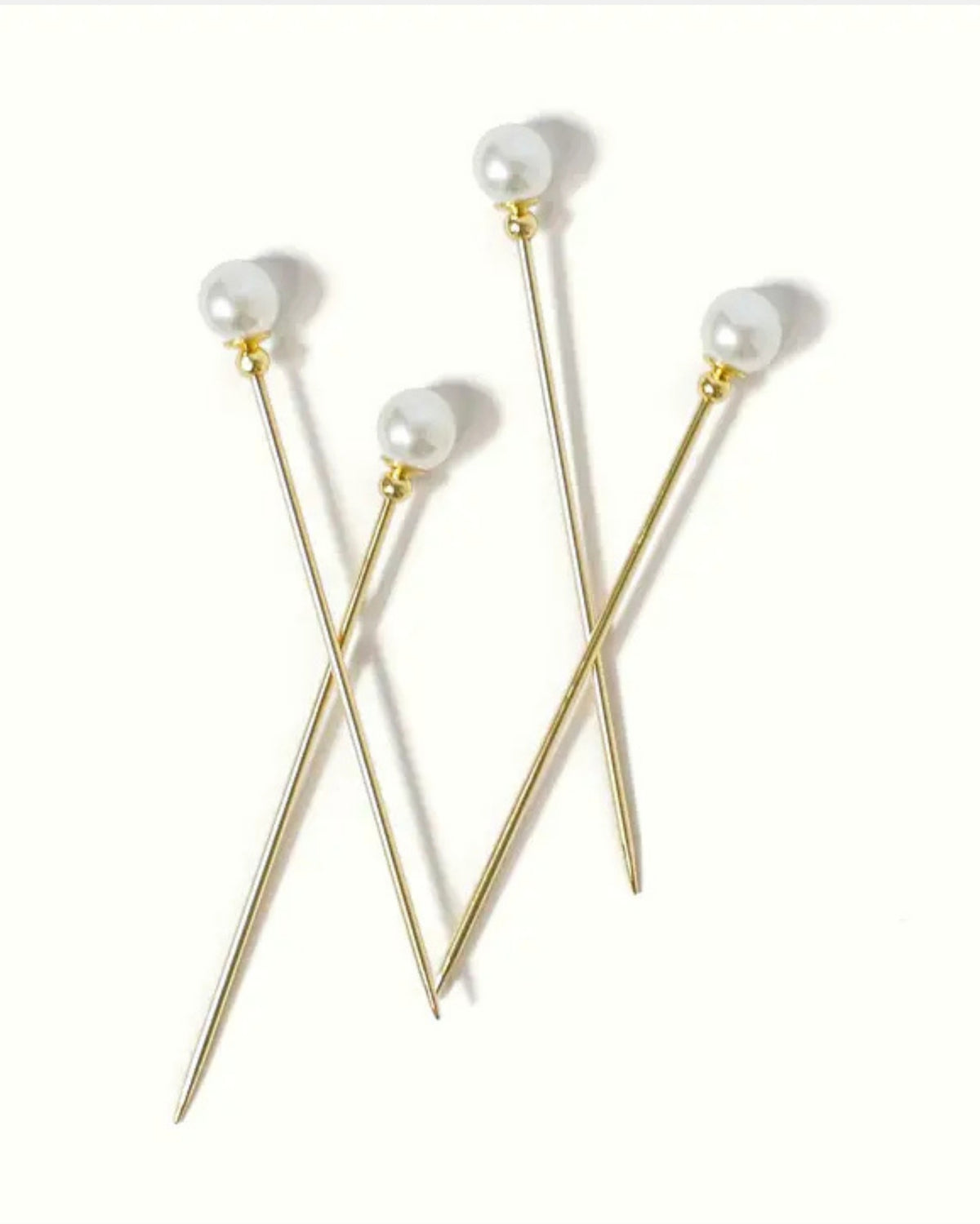 Four gold cocktail picks with white faux-pearl tops arranged on a white background.