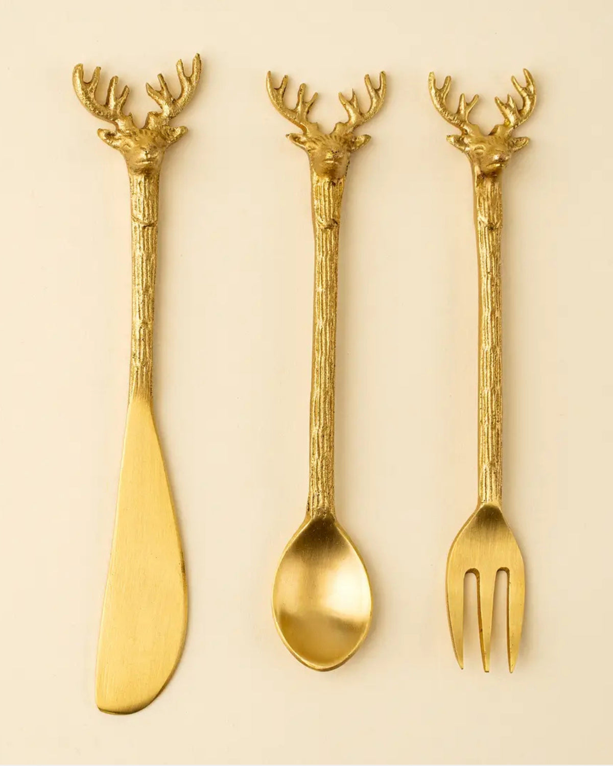 Three gold-colored cheese tools with stag head handles: a spreader, spoon, and fork.