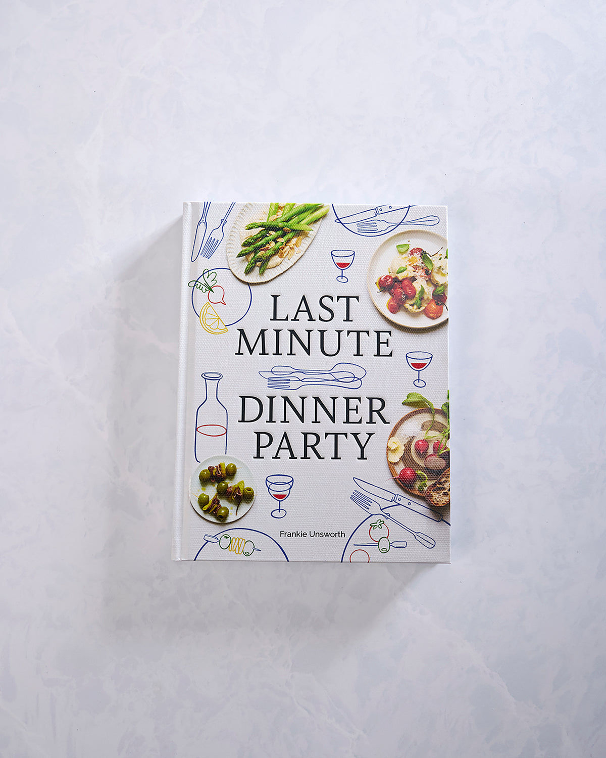 Closed cookbook with a white cover illustrated with plated food, utensils, wine glasses, and the title “Last Minute Dinner Party” by Frankie Unsworth.
