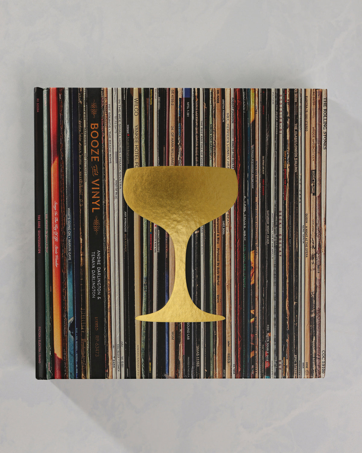 Booze & Vinyl book closed on a stack of vinyl records, with a gold cocktail-glass design on the cover.