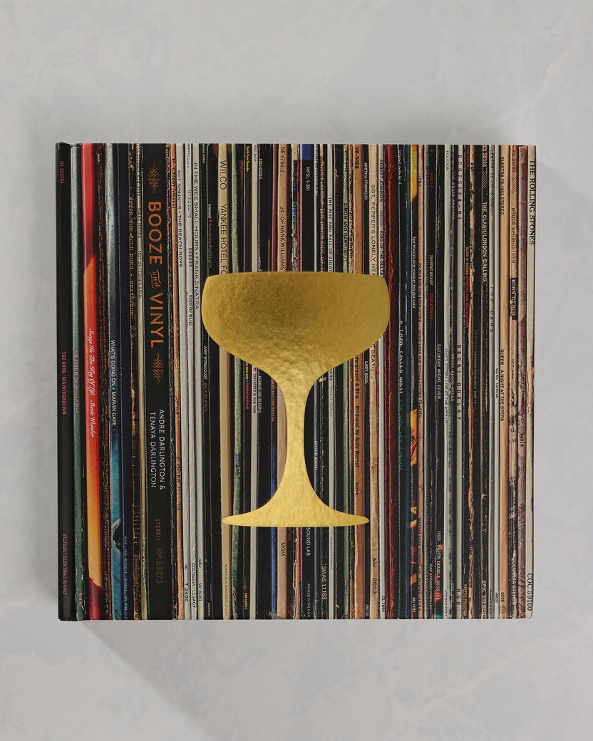 Booze & Vinyl book closed on a stack of vinyl records, with a gold cocktail-glass design on the cover.