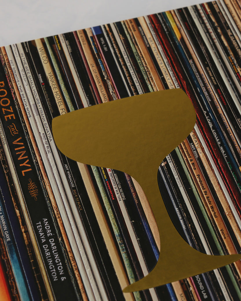 Close-up of the Booze & Vinyl cover’s gold cocktail-glass design over rows of vinyl records.