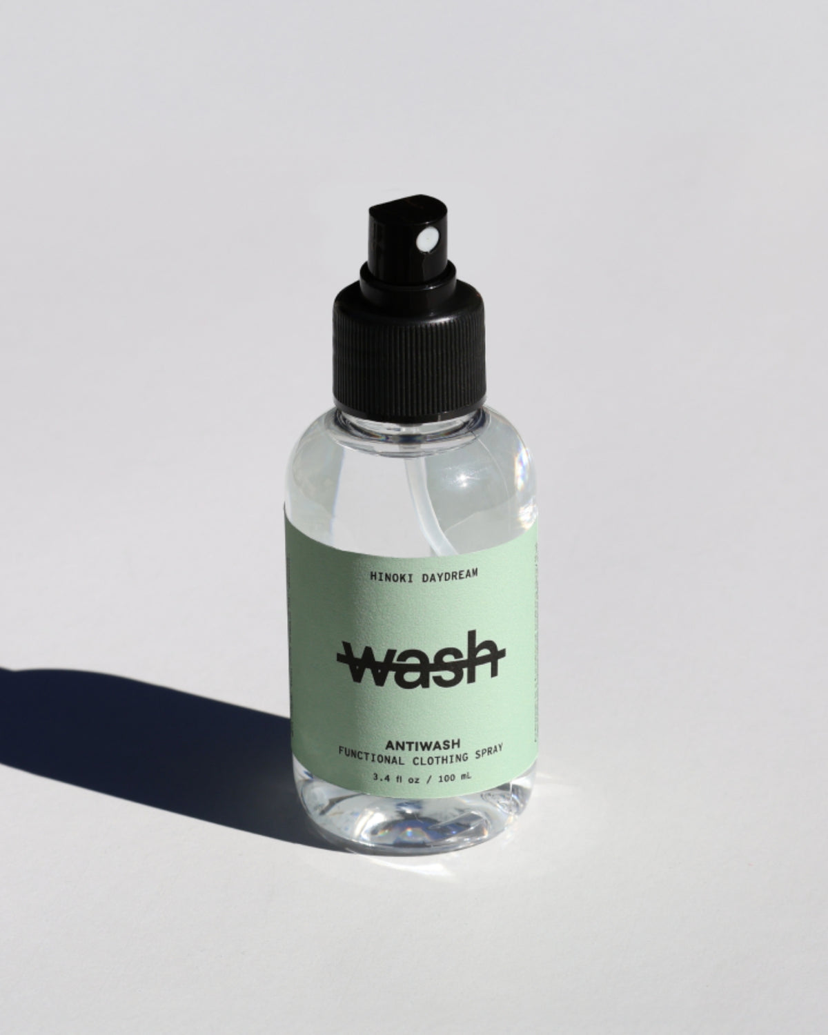 Clear spray bottle of Hinoki Daydream Antiwash functional clothing spray on a white surface.