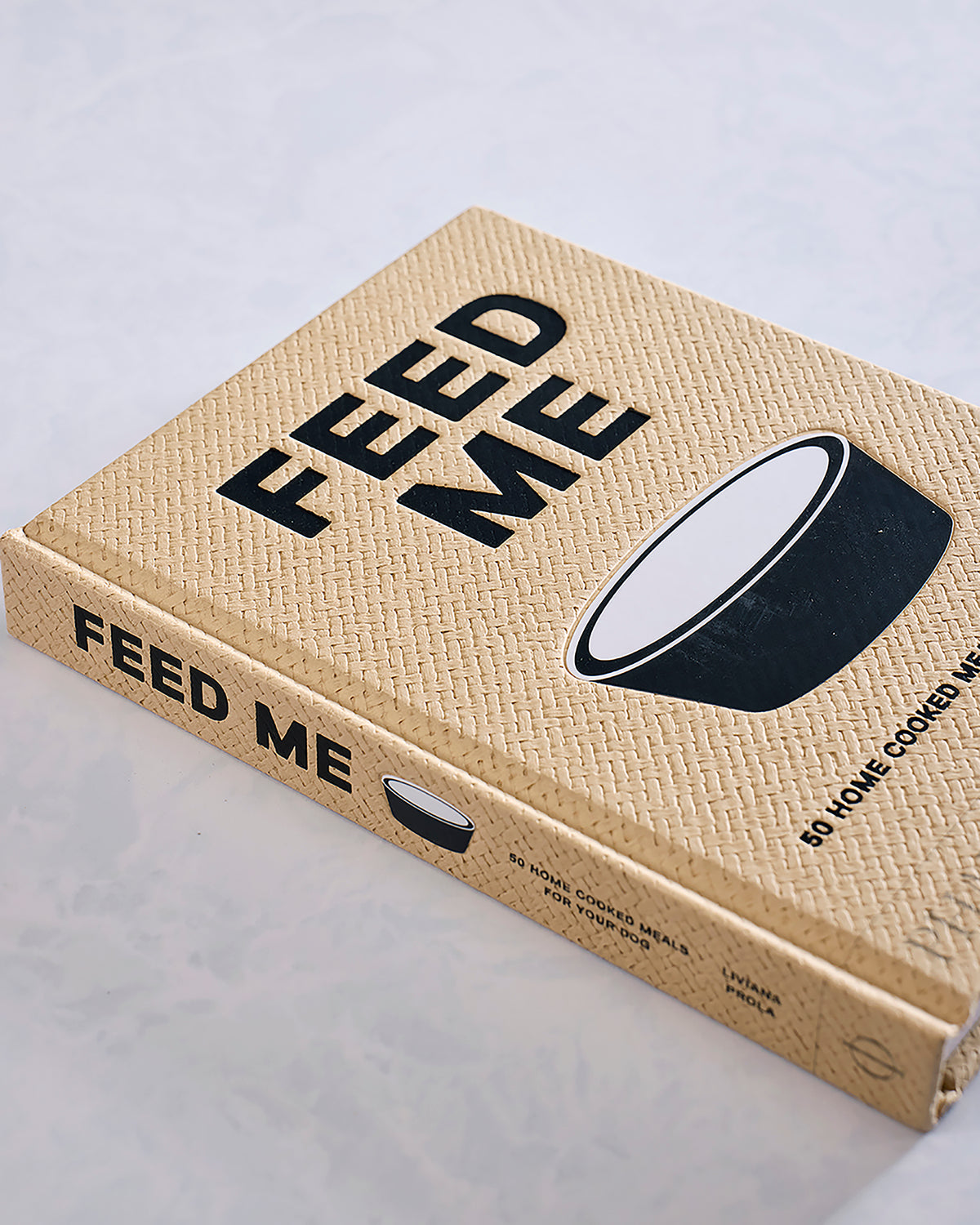 Angled view of the Feed Me cookbook, showing a bowl illustration and the wording 50 home cooked meals for your dog.