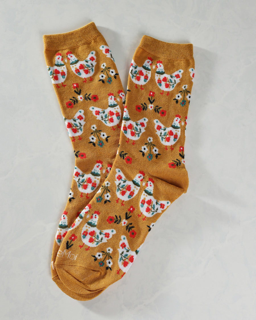 Pair of mustard crew socks covered with repeating white chickens, small flowers, and floral motifs.