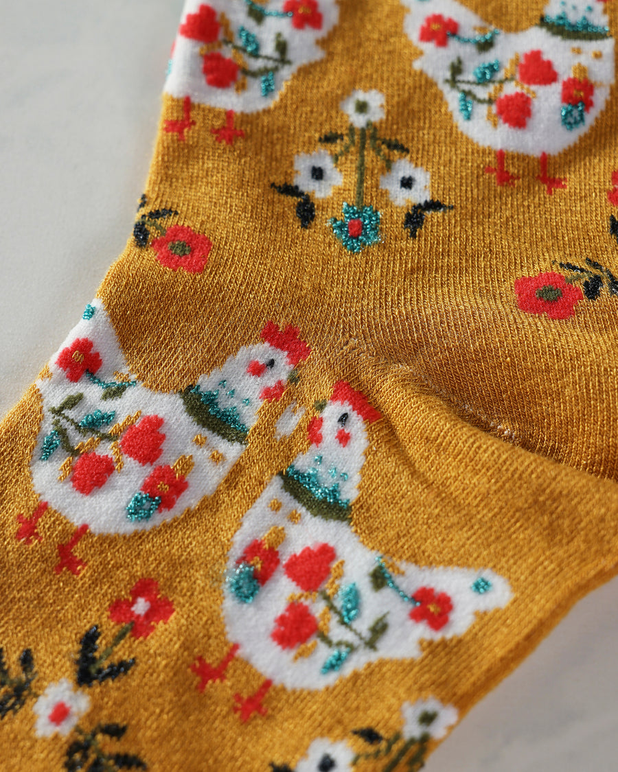 Close-up of mustard County Chick crew sock showing colorful chicken and floral motifs.