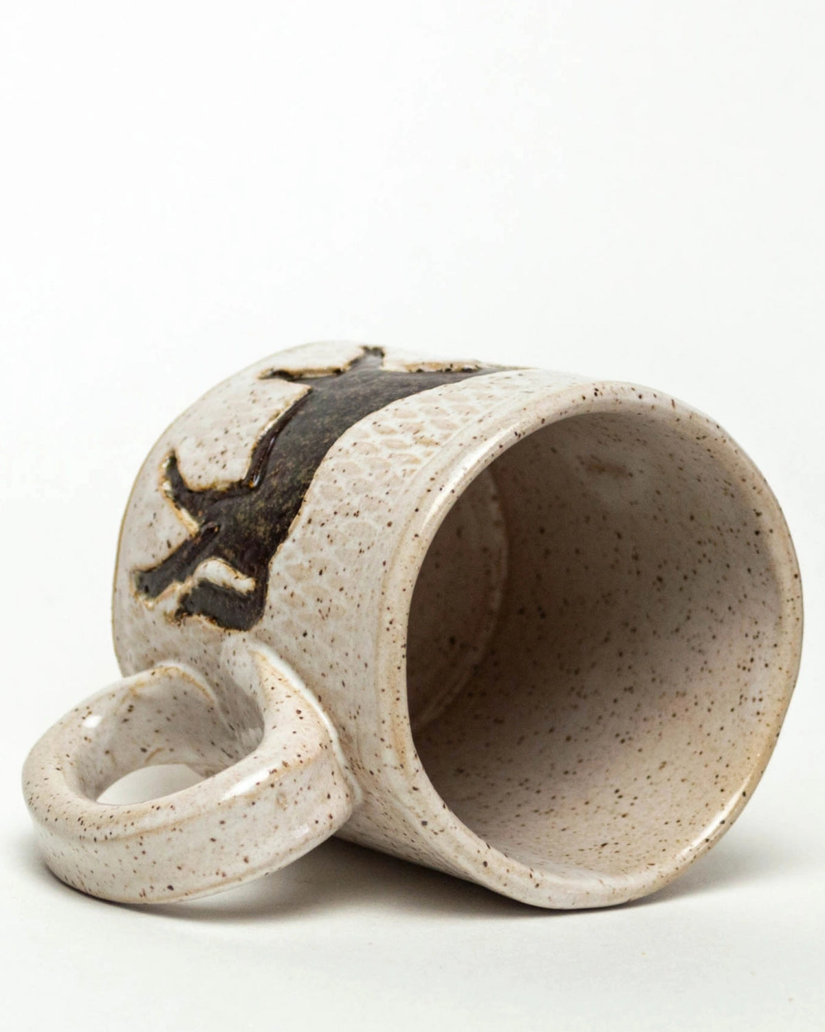 Ivory speckled ceramic mug lying on its side, showing the interior, handle, and dark horse design.