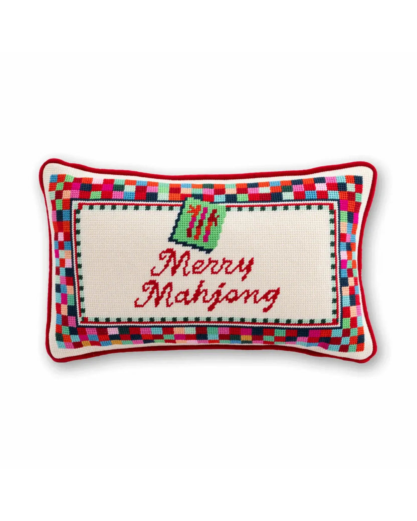 Front of a needlepoint pillow with a colorful patchwork border and the words “Merry Mahjong” in red script.