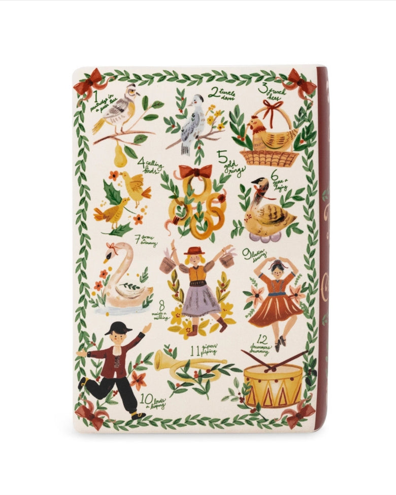 Front view of an ivory ceramic book-shaped vase with a Twelve Days of Christmas illustration, leafy border, and wide top opening.