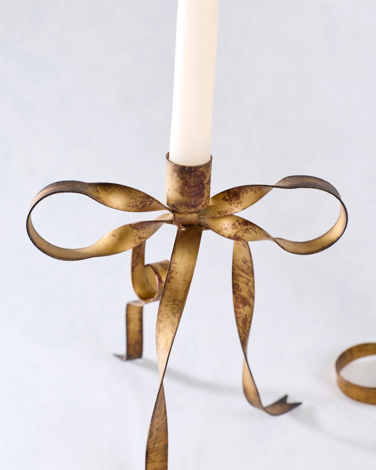 Close-up of the larger brass bow-shaped taper candle holder with a white taper candle.