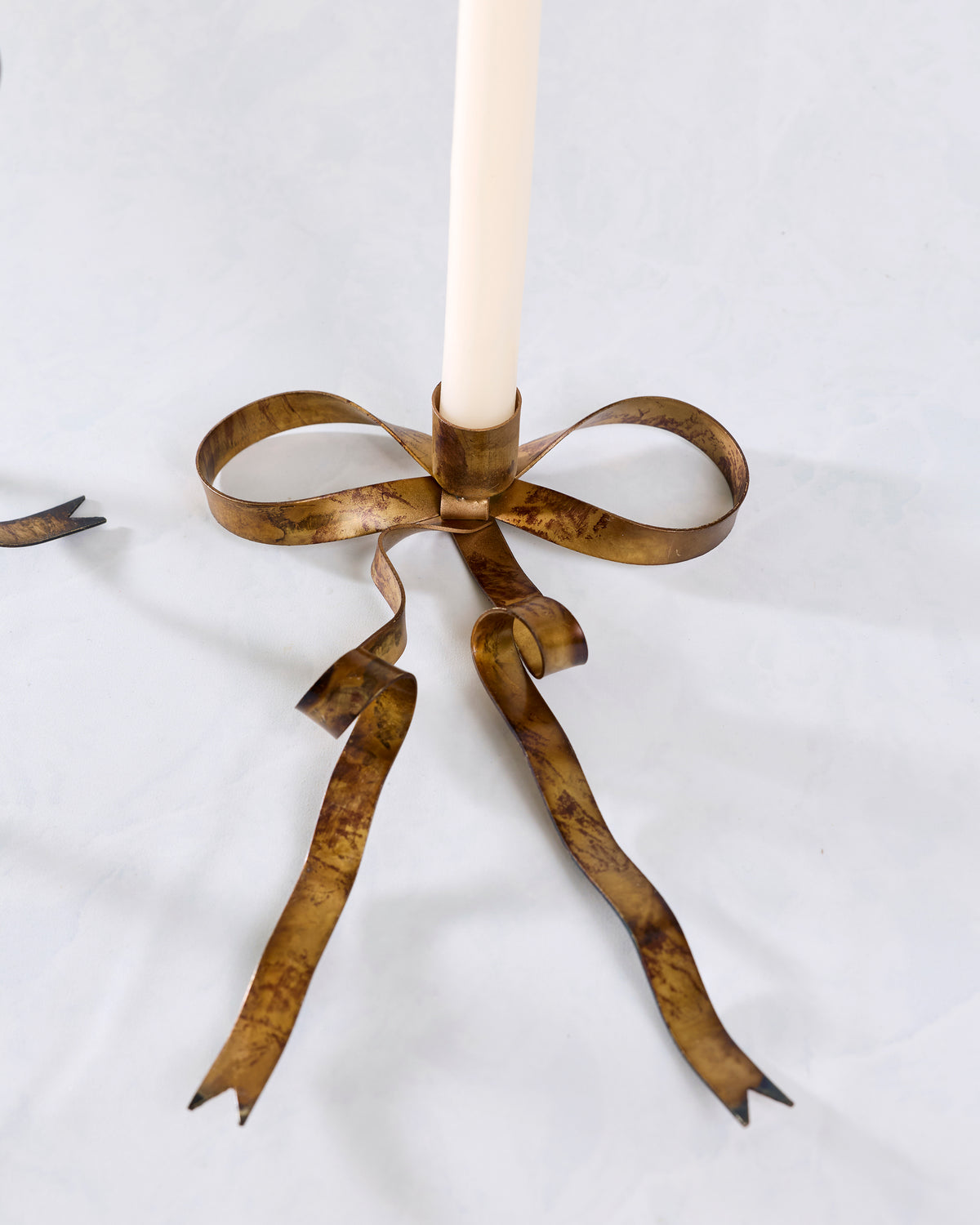 Close-up of the smaller brass bow-shaped taper candle holder with a white taper candle.