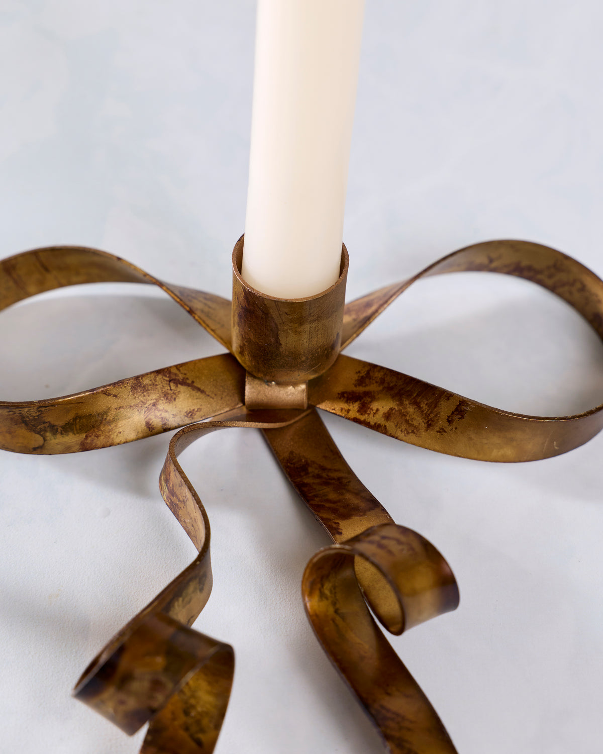 Close-up of an antique brass bow-shaped taper candle holder with a white taper candle inserted.