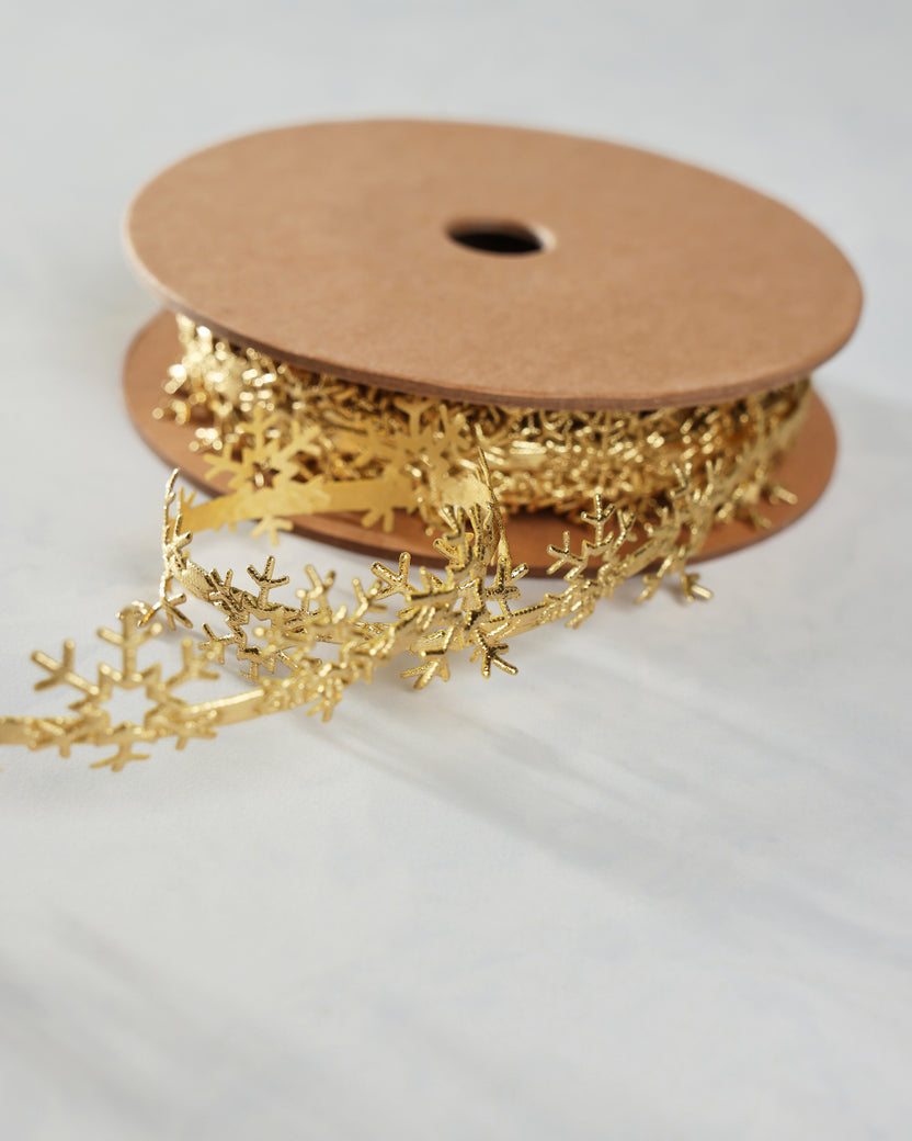 Roll of gold snowflake trim with a length of trim unspooled across the surface.