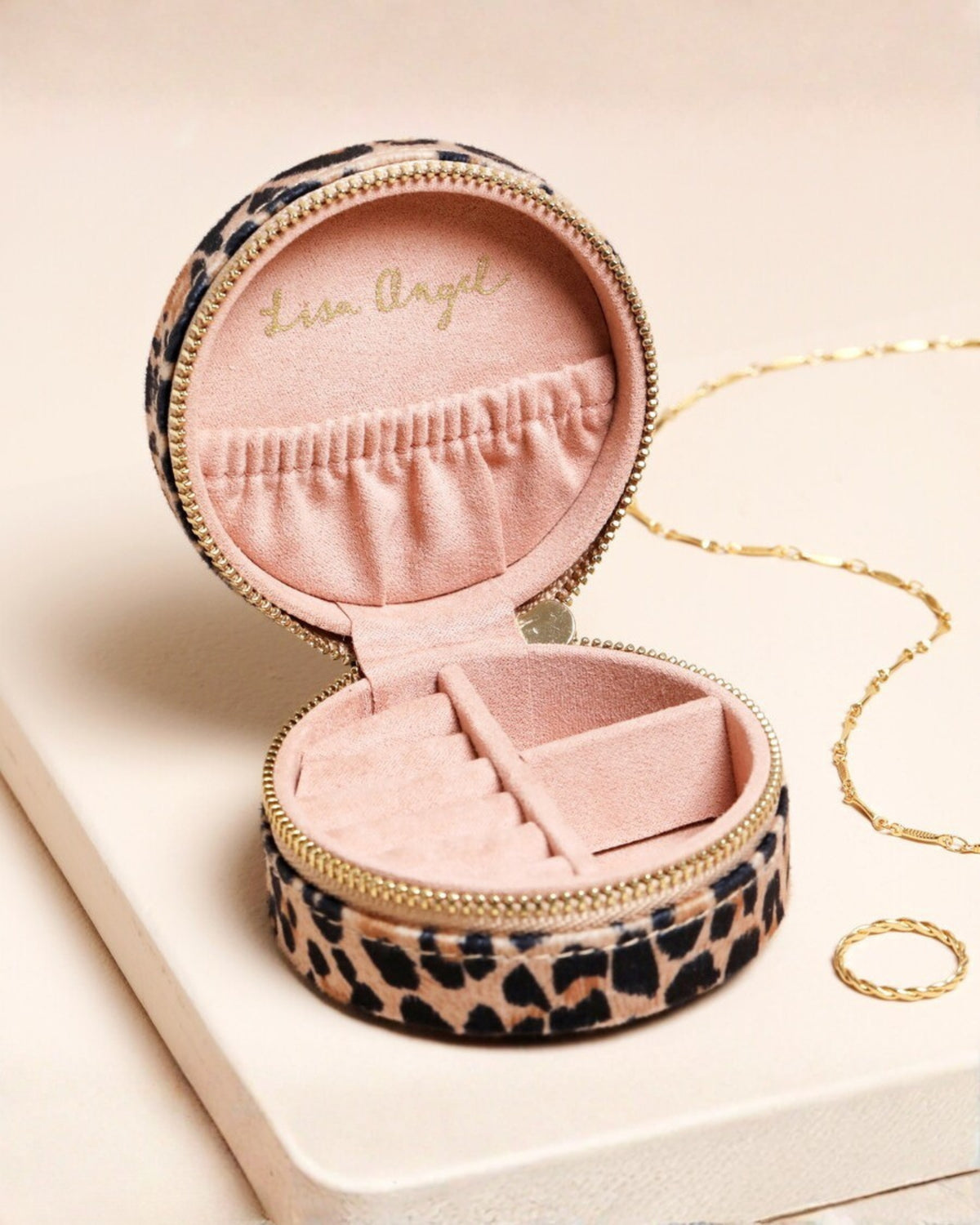 Open round leopard-print travel jewelry case showing a pink interior with ring rolls and compartments.