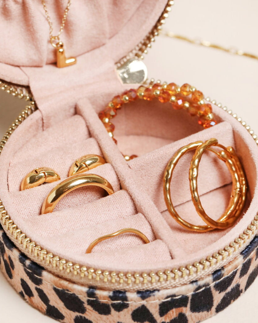 Open leopard-print round travel jewelry case displaying gold-tone jewelry, including rings, hoop earrings, bracelets, and a pendant necklace.