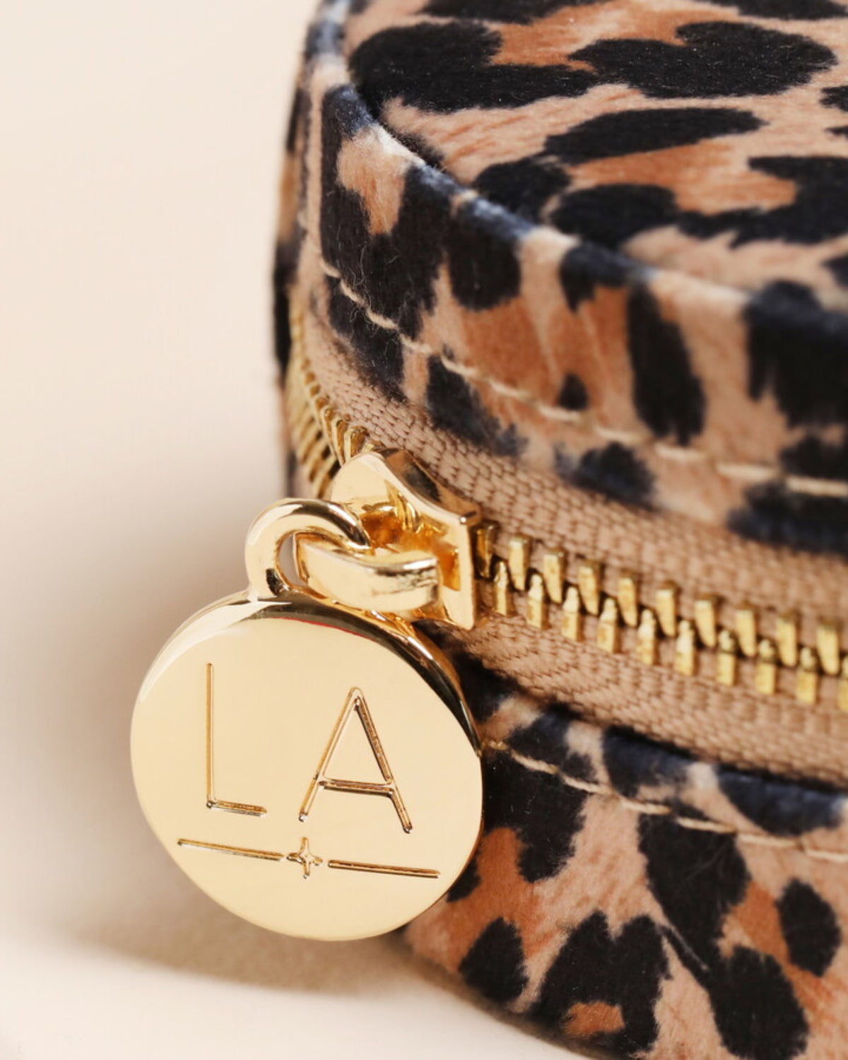 Close-up of the leopard-print jewelry case showing its gold zipper, clasp, and round LA tag.