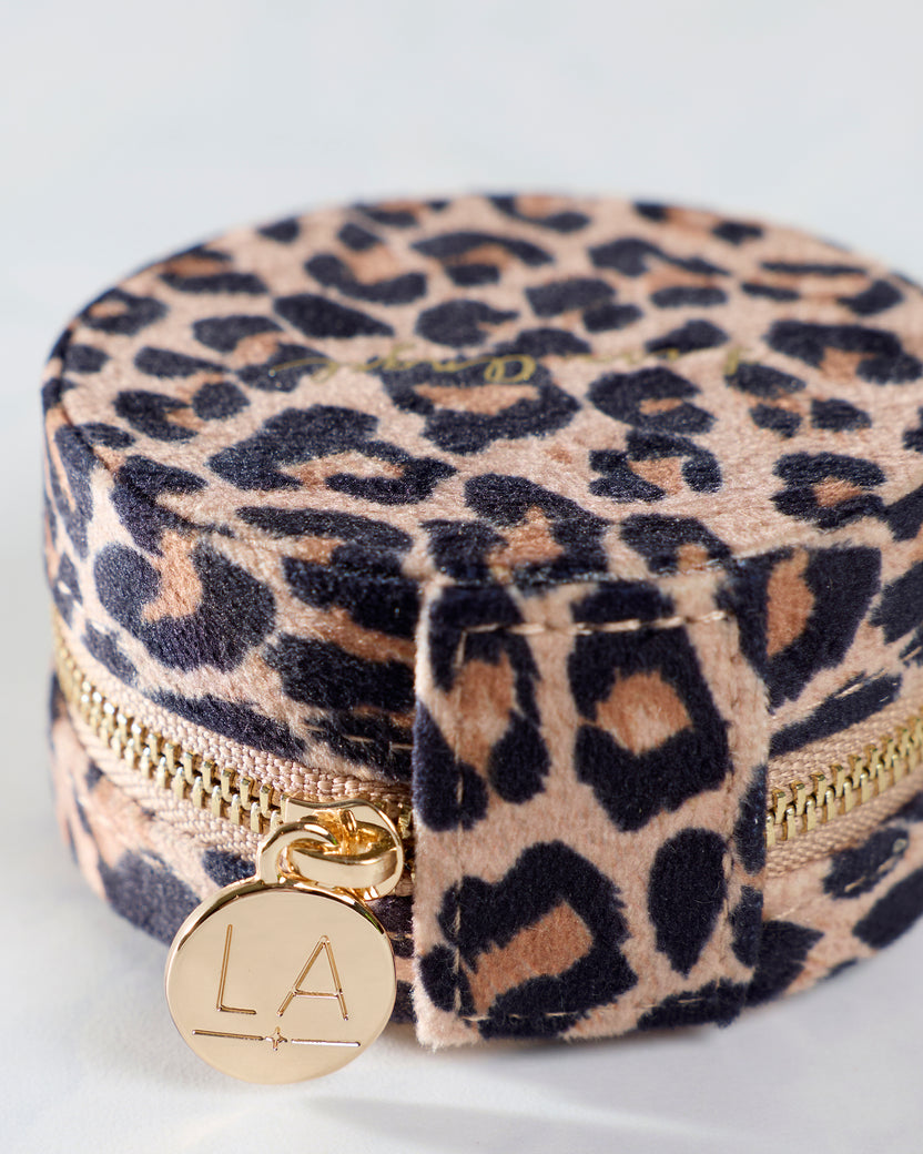 Close-up of a leopard print travel jewelry case showing its zipper pull, fabric strap, and round LA charm.