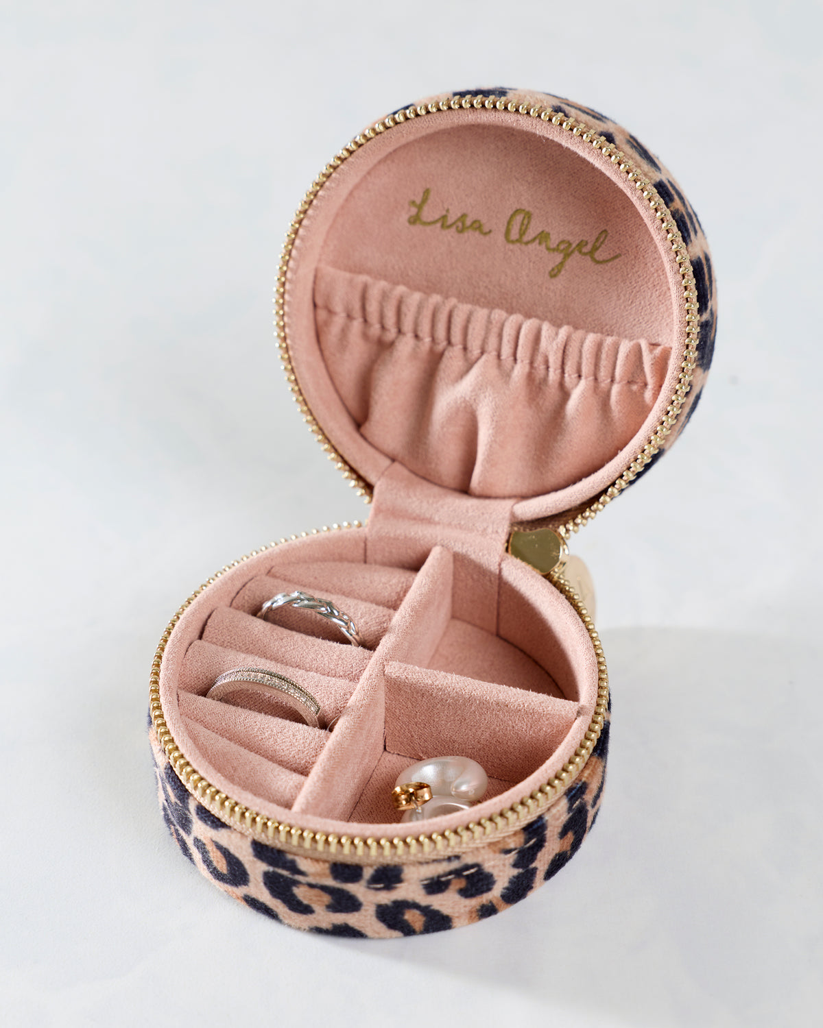 Open leopard-print round travel jewelry case showing ring slots, a divided compartment, and a small pouch inside.