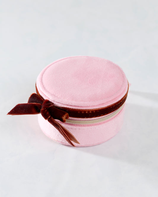 Closed round pink travel jewelry case with a burgundy bow and zipper.
