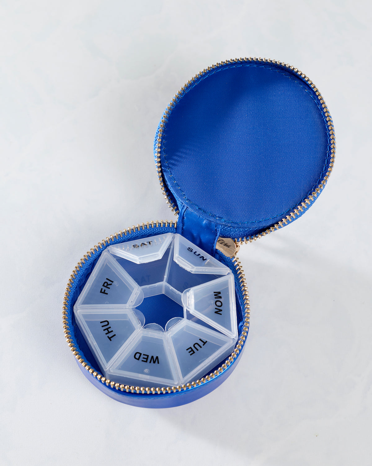 Open blue round pill case containing a removable seven-compartment organizer labeled for each day of the week.