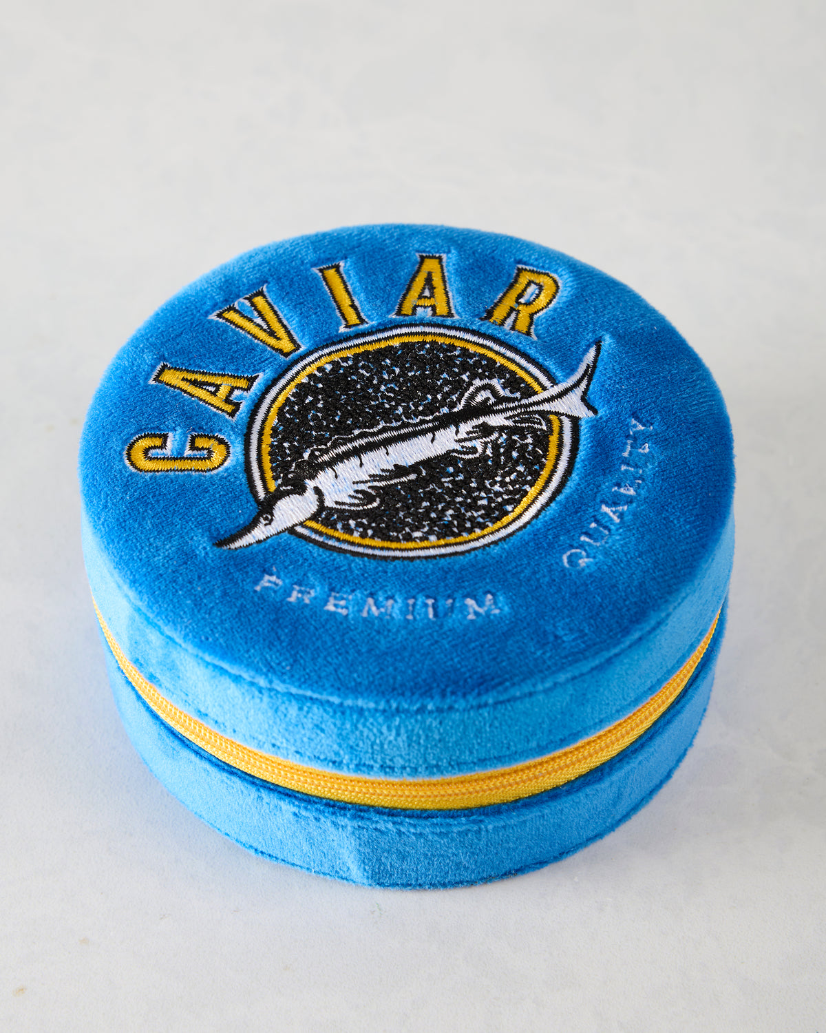 Closed blue velvet jewelry zip case with embroidered swordfish emblem and yellow zipper.