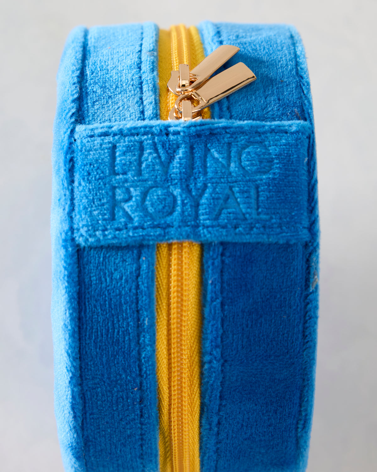 Side view of the blue velvet jewelry zip case showing its yellow zipper and embossed Living Royal branding.