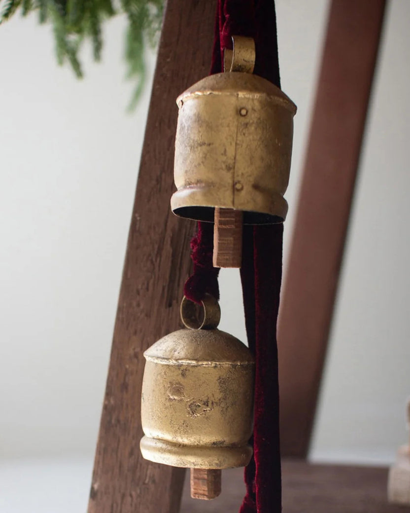 Close-up of two gold jingle bells attached to a maroon ribbon.