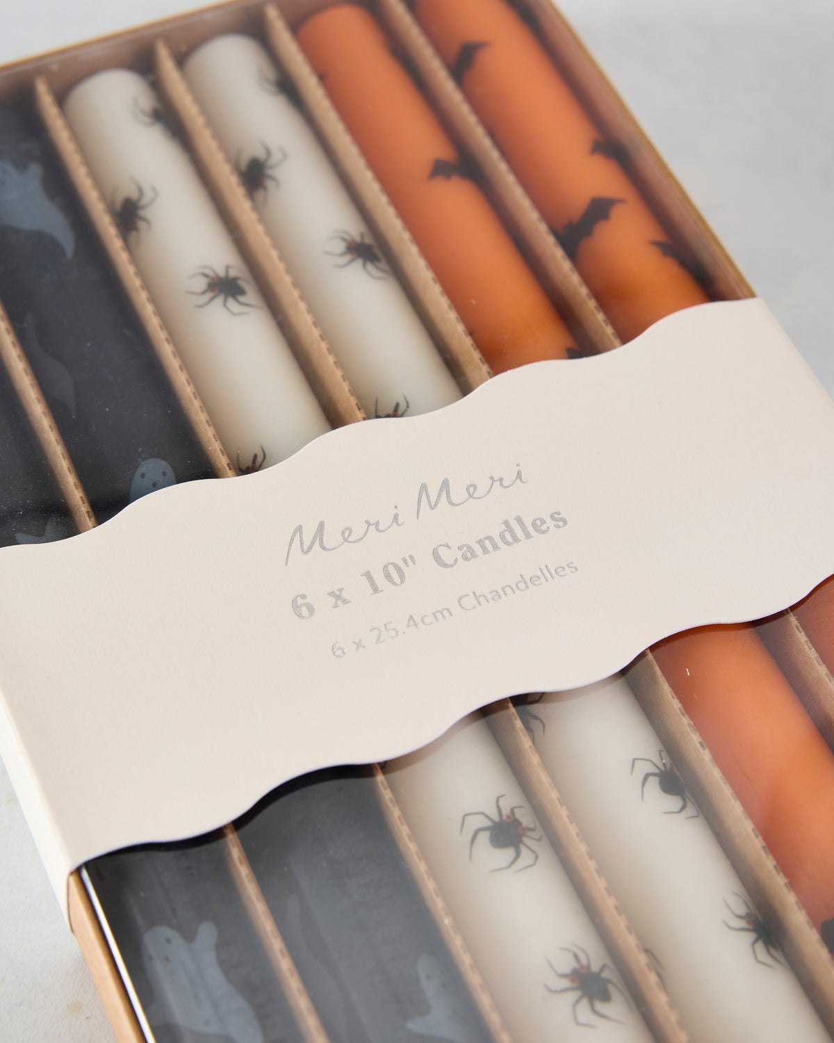 Angled close-up of the boxed Halloween taper candle set showing black ghost, ivory spider, and orange bat designs.